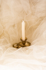 a golden candelabra with a white candle on a white tulle cloth
