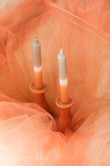 Two candles in salmon and gray colors on pink tulle cloth