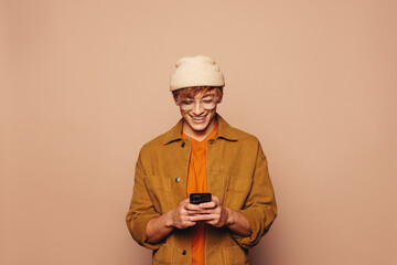 Cheerful young man smiling while reading messages on a smartphone against a vibrant peach background
