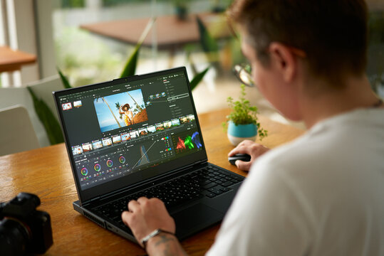 Professional video colorist adjusts footage colors on laptop in bright office. Creative industry editor works on film grading, enhances visual appeal. Expert uses software for post-production.