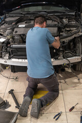 A man is kneeling down to work on a car engine