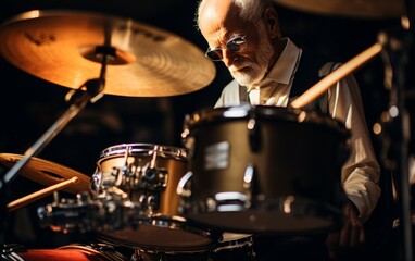 Naklejka premium A man is playing drums in a dark room. He is wearing a vest and glasses. The drums are in front of him and there are two other drums in the background