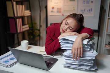 Tired Asian business woman Stress from paperwork, headache, sleepiness on piles of documents. Bored from sitting at a desk for a long time and has office syndrome.
