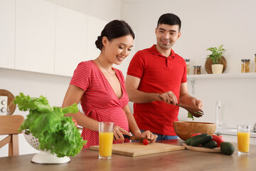 Happy young pregnant couple cooking in kitchen