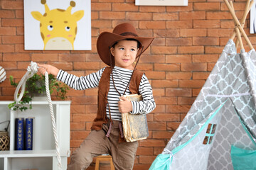 Cute little cowboy with adventure book and rope at home
