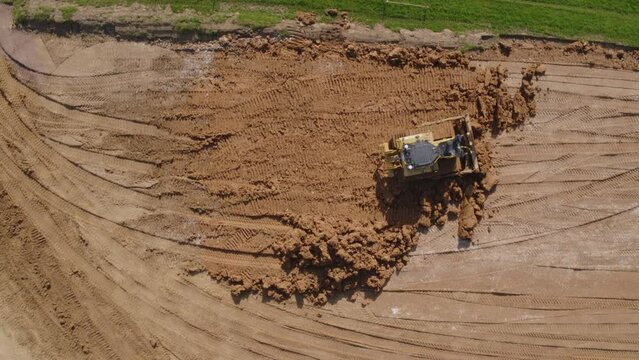 Top down of a bull dozer flattening out earth on a heavily worked construction site
