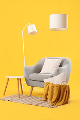 Cozy grey armchair with cushions, lamps and coffee table on yellow background