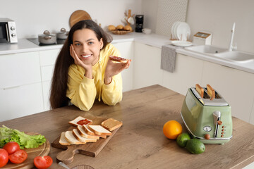 Young beautiful happy woman eating tasty toasts with jam and peanut butter in kitchen