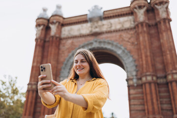 Young female tourist visiting Barcelona triumphal arch. Traveling woman taking selfie outdoors....