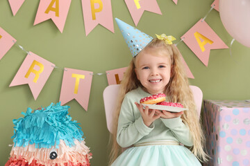 Cute little girl in party hat with donuts celebrating Birthday at home