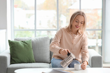 Pretty young woman pouring espresso from geyser coffee maker into cup in living room