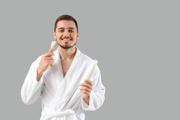 Handsome young man in bathrobe with shaving brush on grey background