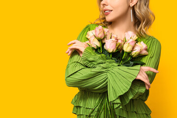 Young woman with bouquet of beautiful roses on yellow background