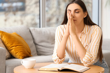 Beautiful woman with Holy Bible praying on sofa at home