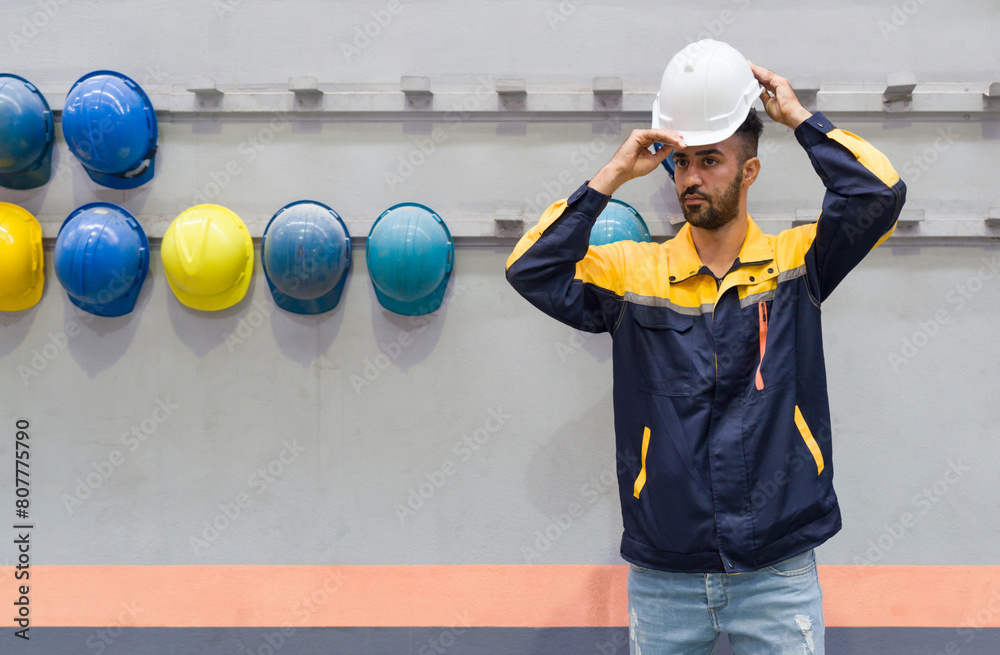 Wall mural young man working in a factory, wearing construction hardhat on his head for safety. concept of work