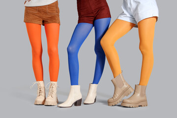 Stylish women in colorful tights wearing different boots on grey background