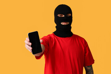 Handsome young man in balaclava with mobile phone on yellow background