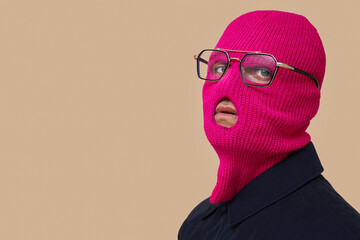 Handsome young man in balaclava with stylish eyeglasses on beige background