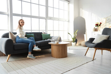 Young woman sitting on sofa near window in living room