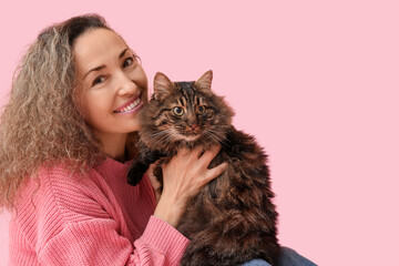 Happy mature woman with cute cat on pink background
