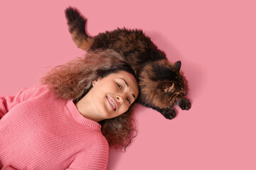 Mature woman with cute cat lying on pink background