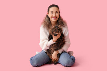 Beautiful mature woman with cute cat sitting on pink background