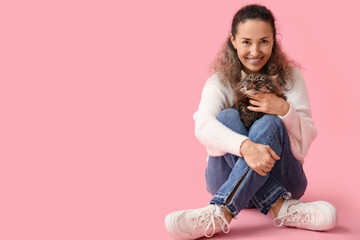 Mature woman with cute cat sitting on pink background