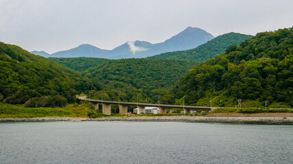 A picturesque view from the sightseeing cruiser overlooking the Horobetsu Bridge at the mouth of the Horobetsu River and Mount Tenchozan in the Shiretoko Peninsula, Hokkaido, Japan.
