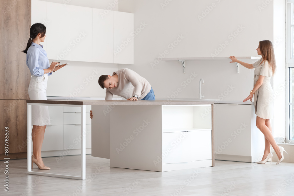 Sticker real estate agent showing young couple kitchen in new house