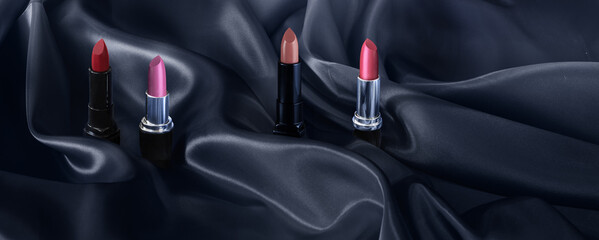 Four lipsticks in various shades rest on a satin cloth