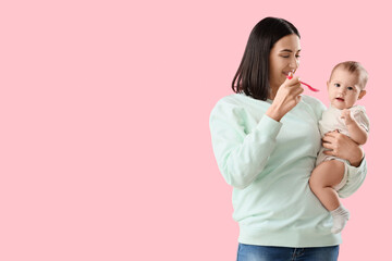 Young woman feeding her little baby with puree on pink background