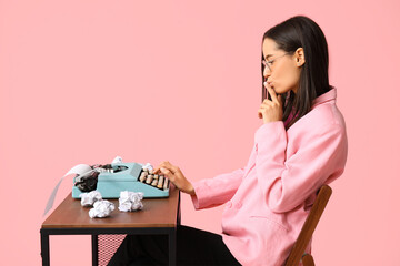 Beautiful young woman working with vintage typewriter at table on pink background