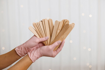 Woman holding many wax wooden spatulas. The young woman is wearing beige clothing and in pink...