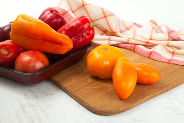 Cutting board with assort of different tomatoes and bell pepper on white wooden background..