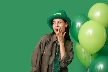 Beautiful young woman in leprechaun hat with air balloons on green background. St. Patrick's Day...