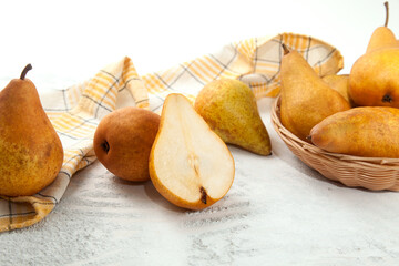 Whole and halves of pears, wicker basket and yellow kitchen towel on white wooden background..