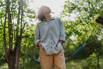 Cheerful young Caucasian woman enjoying summer standing in a green garden in the sun