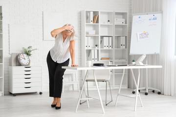 Stressed mature businesswoman experiencing menopause in office