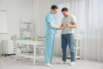 Obraz premium Male nutritionist measuring man's waist in clinic
