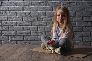 Homeless little girl sitting near grey brick wall