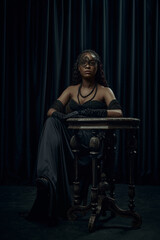 Confident, statuesque African-American woman seated in classic vintage black dress with mask...