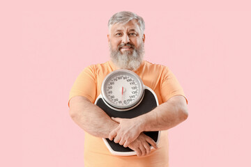 Overweight happy mature man with scales on pink background. Weight loss concept