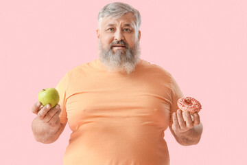 Overweight happy mature man with apple and donut on pink background. Weight loss concept