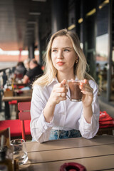 Gen z blonde woman drinks hot chocolate in summer cafe. Tasty beverage and break concept. Generation z people