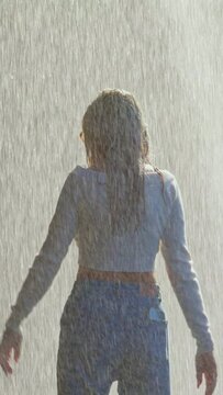 Vertical video: Happy woman dancing in waterfall drops having fun enjoying freedom with arms raised feeling carefree tropical vacation