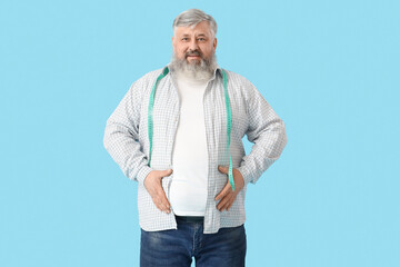 Overweight happy mature man with measuring tape on blue background. Weight loss concept