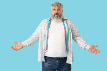 Overweight mature shocked man with measuring tapes on blue background. Weight loss concept