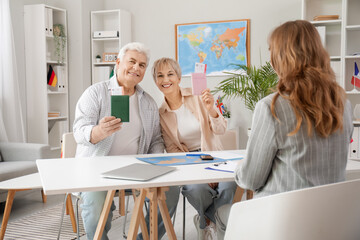 Mature couple with passports sitting at table in travel agency