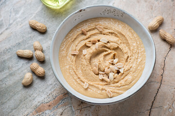 Bowl with freshly made peanut butter on a grey and roseate granite background, horizontal shot