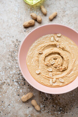 Roseate bowl with peanut butter or paste made from ground, dry-roasted peanuts, vertical shot on a...